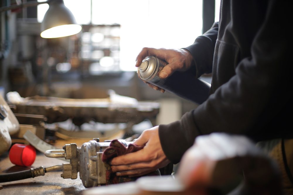 Mechanic spraying an aerosol cleaner on a part at a shop bench