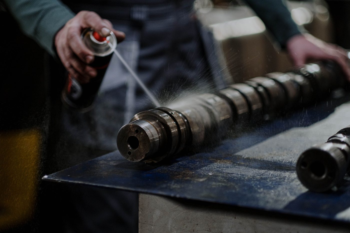 A technician cleaning an engine camshaft at a shop workbench
